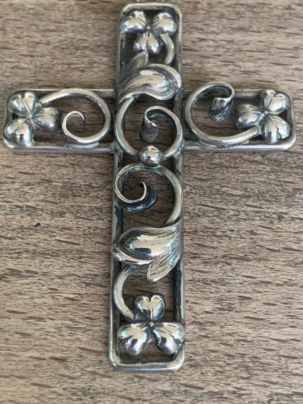 An antique silver cross pendant featuring openwork scrollwork and four-petal floral motifs at the terminals. View IV