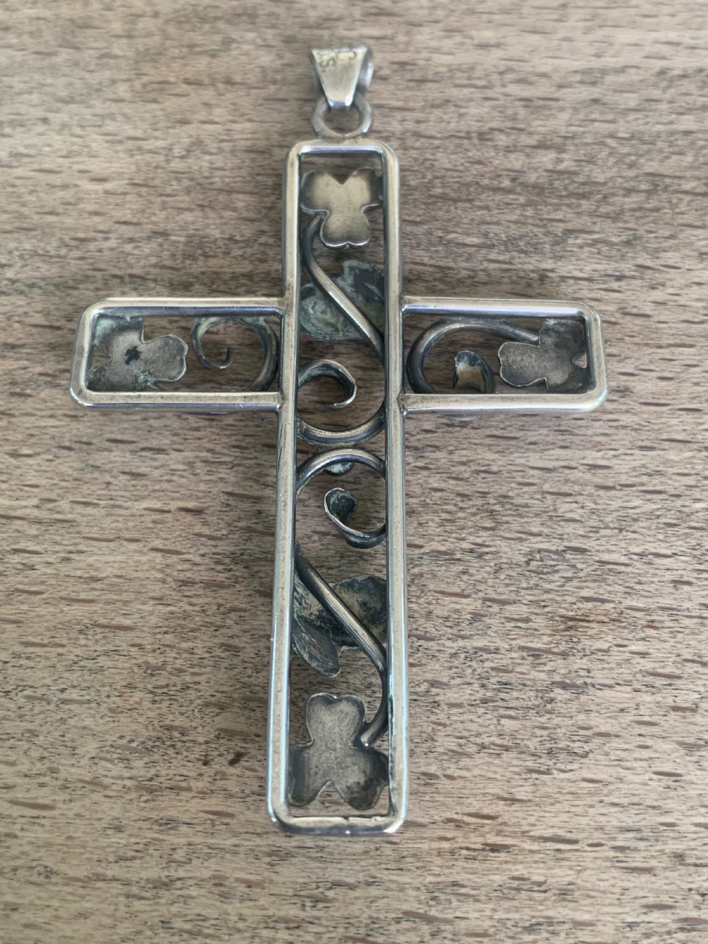 An antique silver cross pendant featuring openwork scrollwork and four-petal floral motifs at the terminals. View V