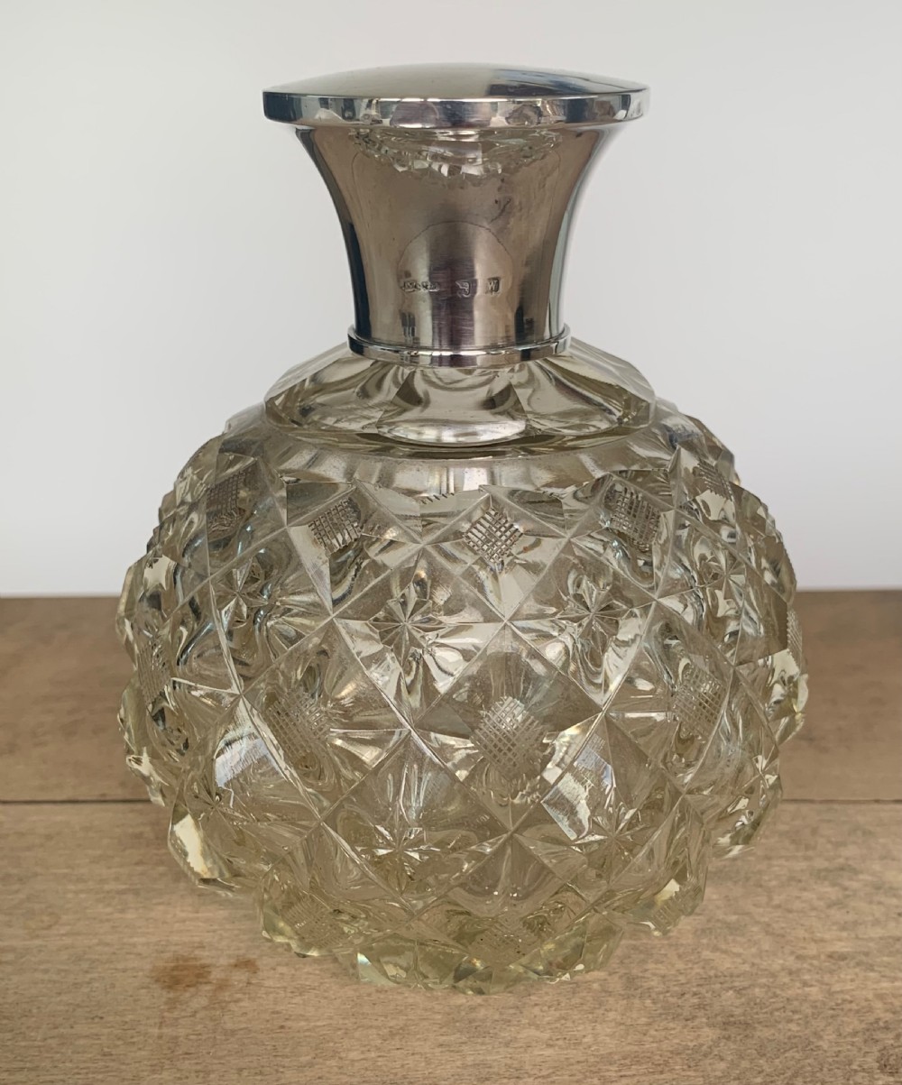 A spherical clear cut glass scent bottle featuring diamond patterns and a polished sterling silver neck collar and lid.