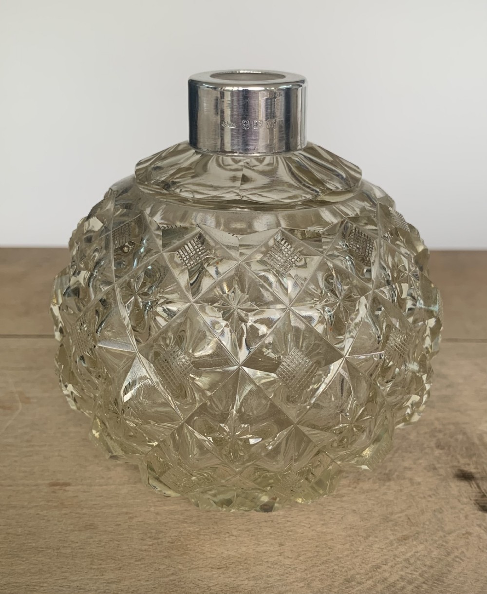 A spherical clear cut glass scent bottle featuring diamond patterns and a polished sterling silver neck collar and lid. View II