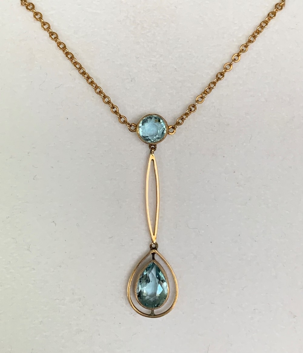 An Edwardian 9ct yellow gold drop necklace featuring a round light blue gemstone linked to a pear-cut gemstone in an openwork frame.