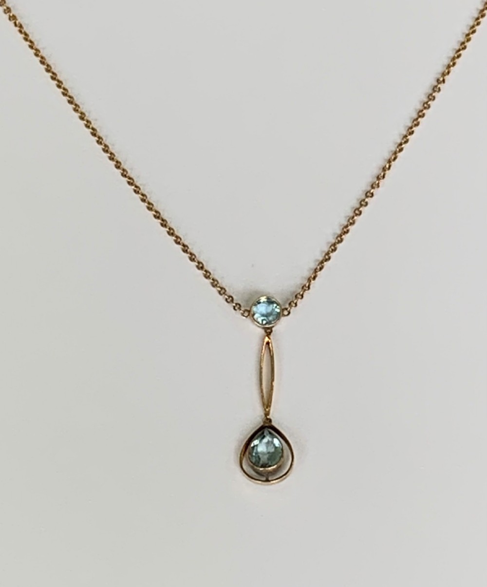 An Edwardian 9ct yellow gold drop necklace featuring a round light blue gemstone linked to a pear-cut gemstone in an openwork frame. View II