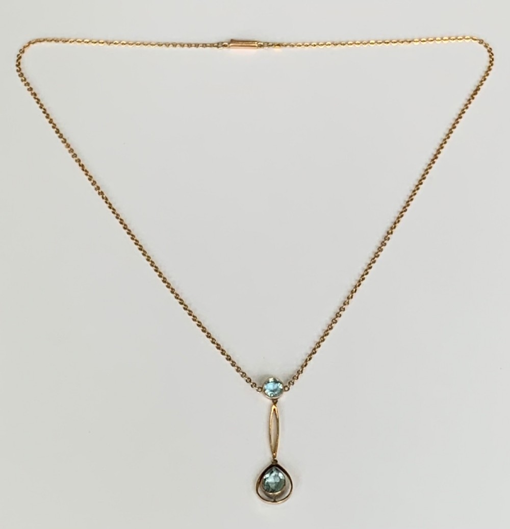 An Edwardian 9ct yellow gold drop necklace featuring a round light blue gemstone linked to a pear-cut gemstone in an openwork frame. View III