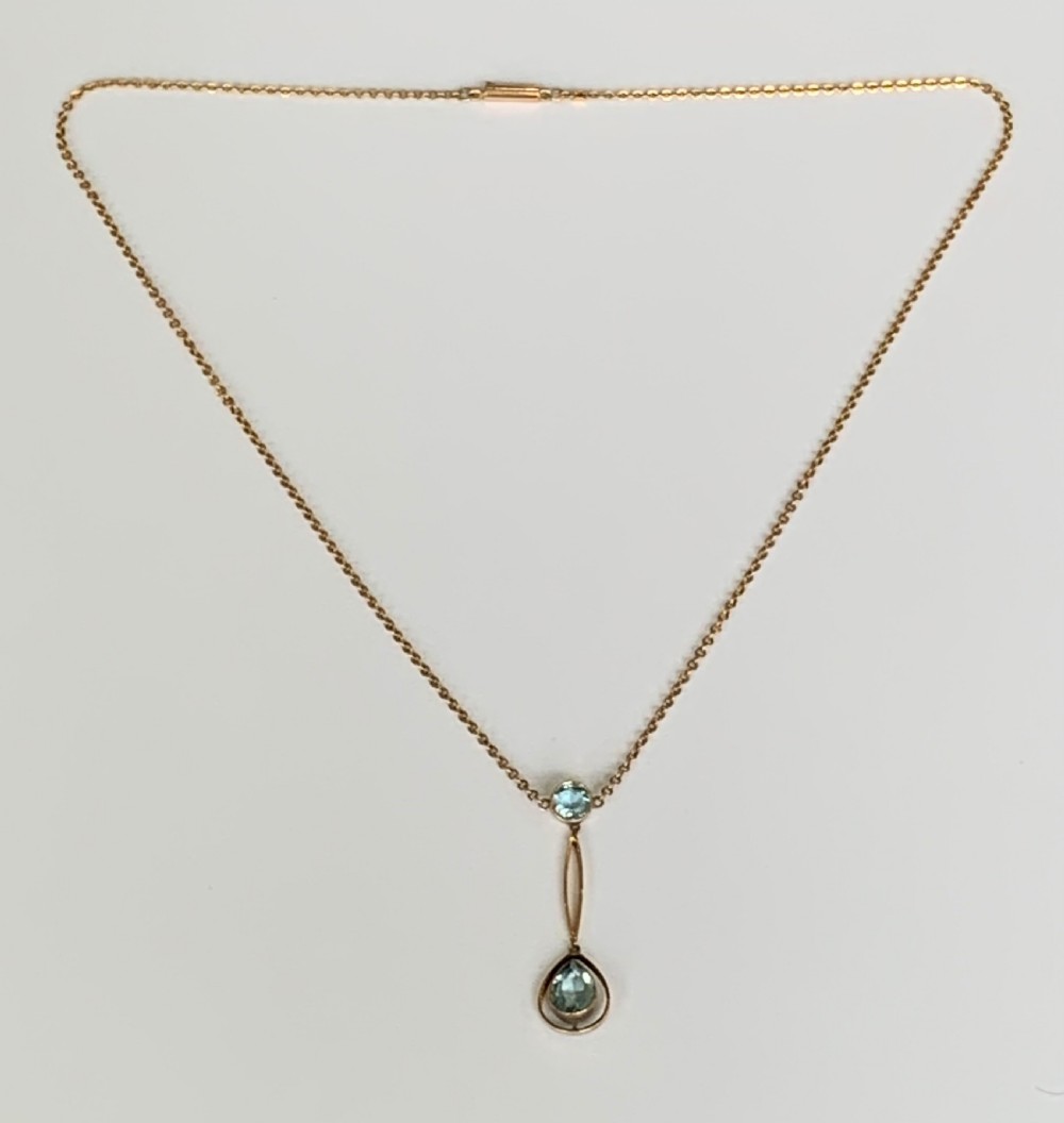 An Edwardian 9ct yellow gold drop necklace featuring a round light blue gemstone linked to a pear-cut gemstone in an openwork frame. View IV