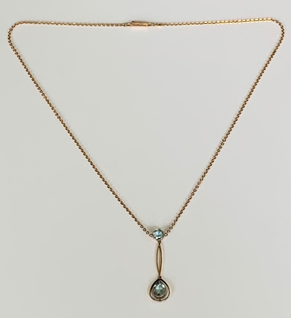 An Edwardian 9ct yellow gold drop necklace featuring a round light blue gemstone linked to a pear-cut gemstone in an openwork frame. View VI