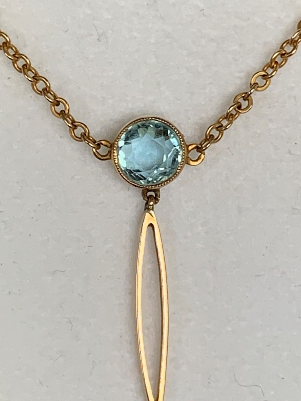 An Edwardian 9ct yellow gold drop necklace featuring a round light blue gemstone linked to a pear-cut gemstone in an openwork frame. View VII