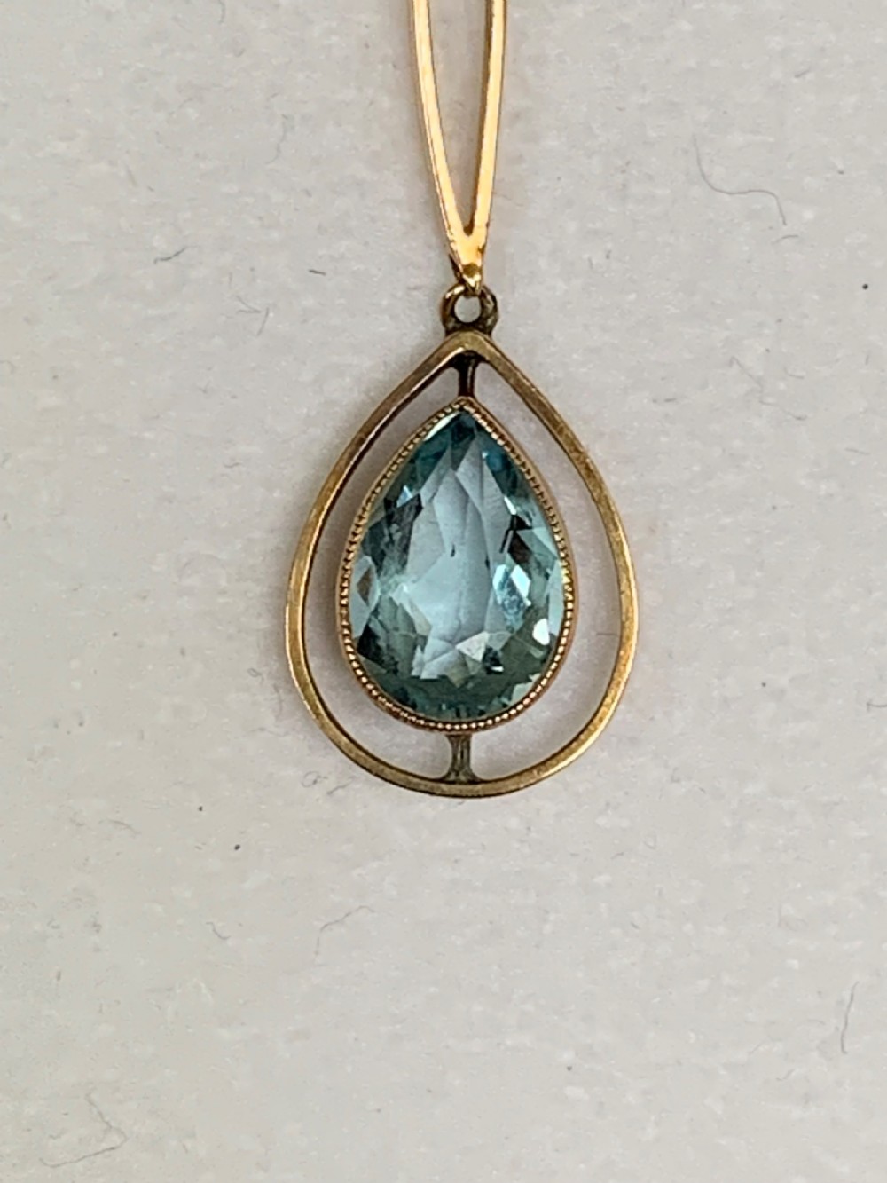 An Edwardian 9ct yellow gold drop necklace featuring a round light blue gemstone linked to a pear-cut gemstone in an openwork frame. View VIII