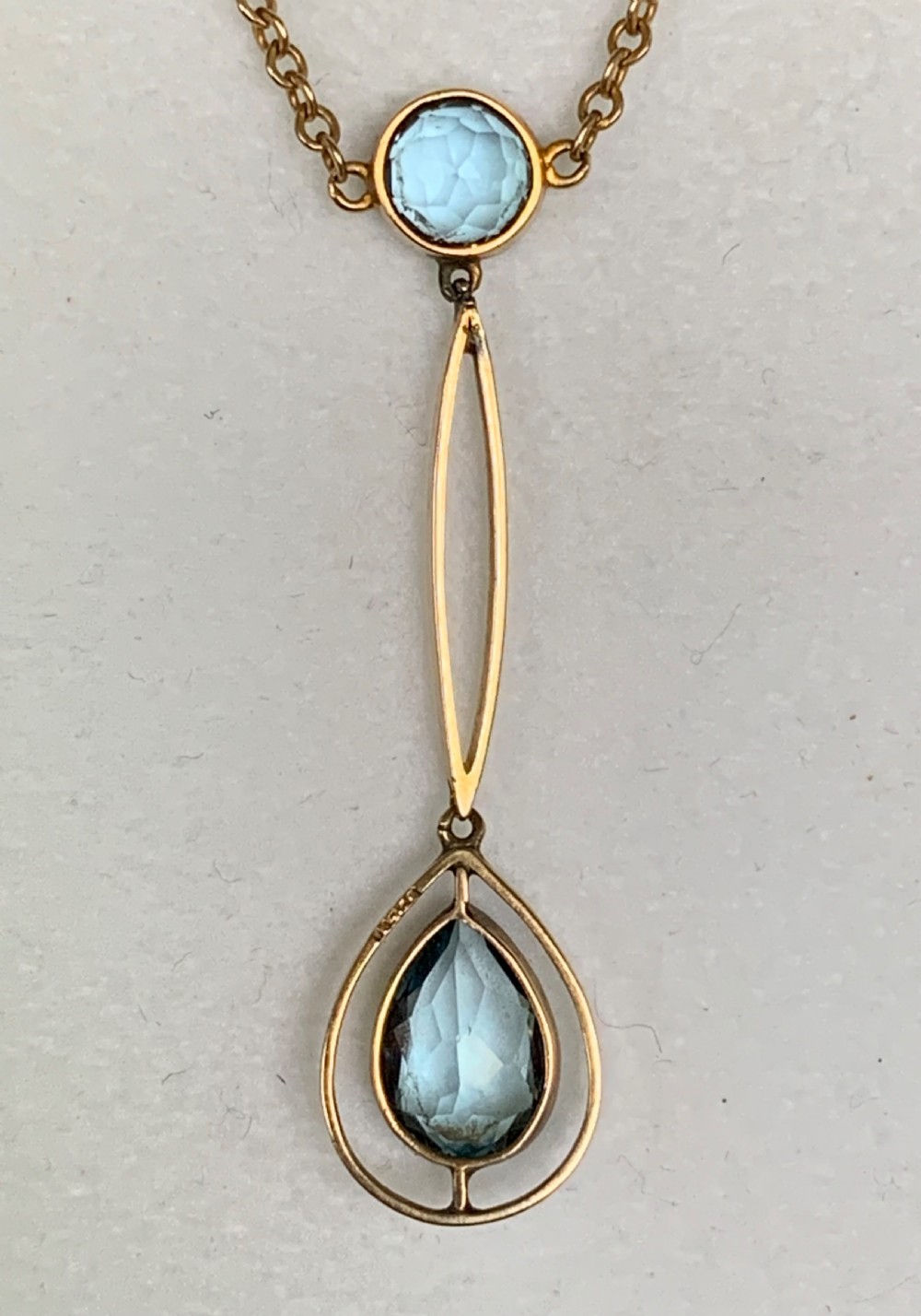 An Edwardian 9ct yellow gold drop necklace featuring a round light blue gemstone linked to a pear-cut gemstone in an openwork frame. View IX