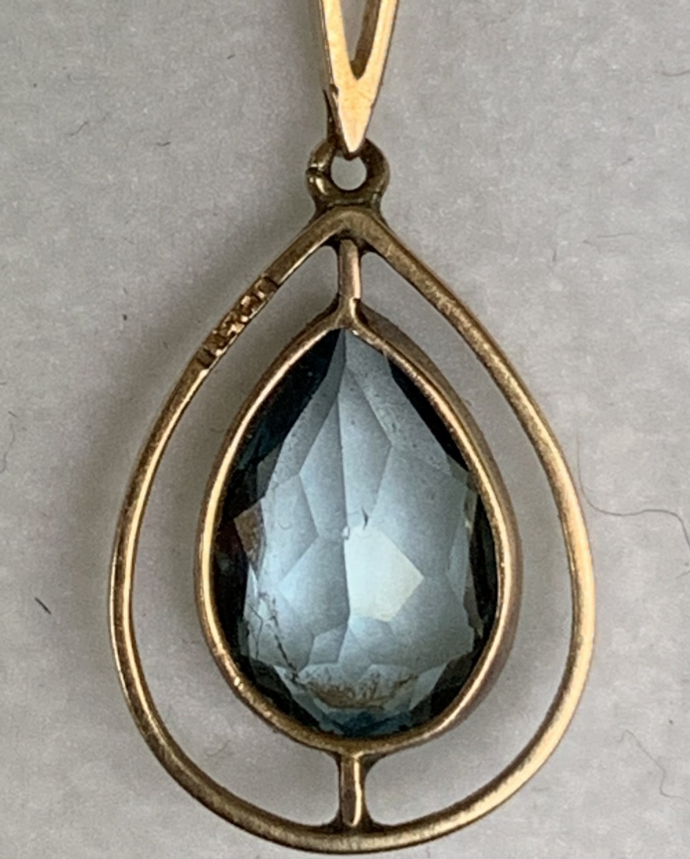 An Edwardian 9ct yellow gold drop necklace featuring a round light blue gemstone linked to a pear-cut gemstone in an openwork frame. View X