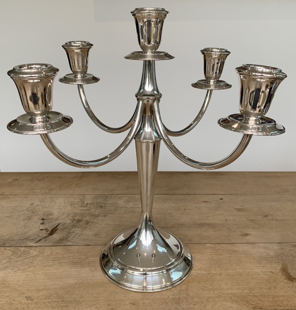A polished silver candelabra featuring a central candle socket surrounded by four sweeping curved branches resting on a stepped round base. View IV