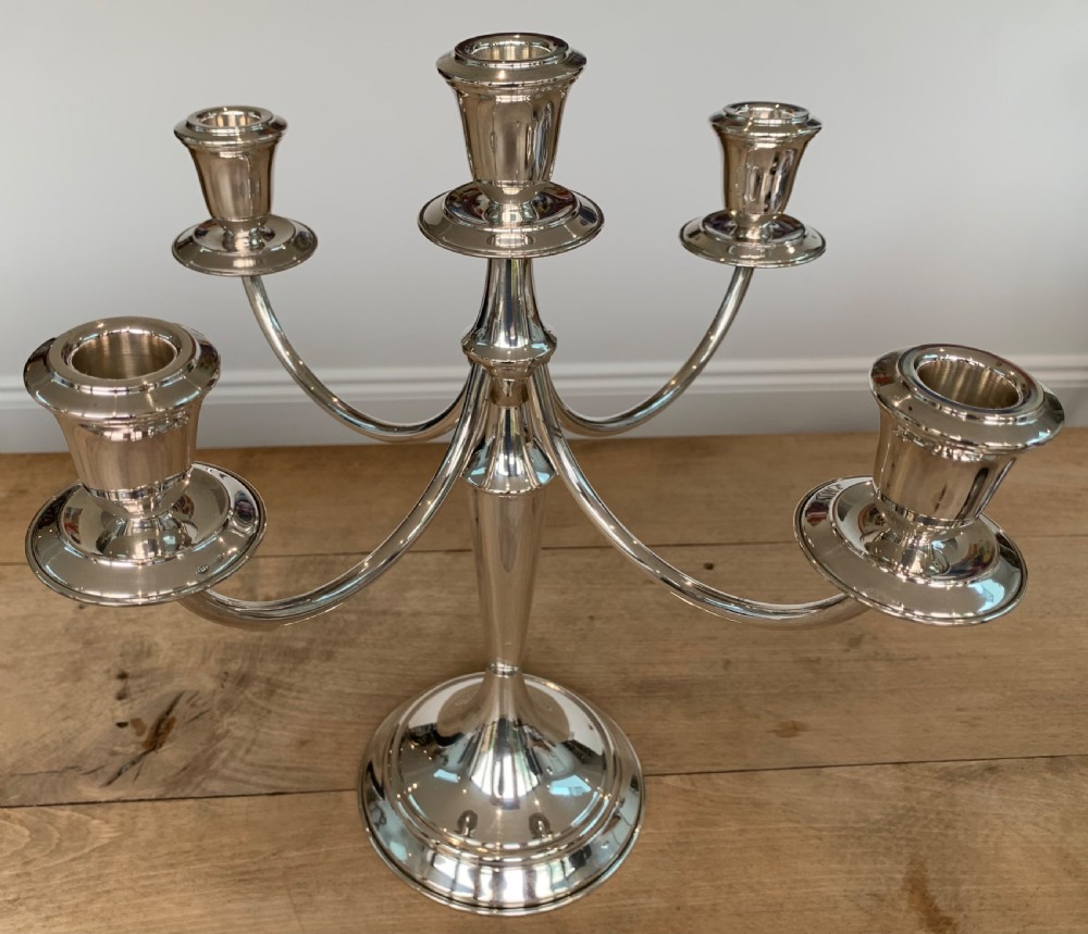 A polished silver candelabra featuring a central candle socket surrounded by four sweeping curved branches resting on a stepped round base. View V
