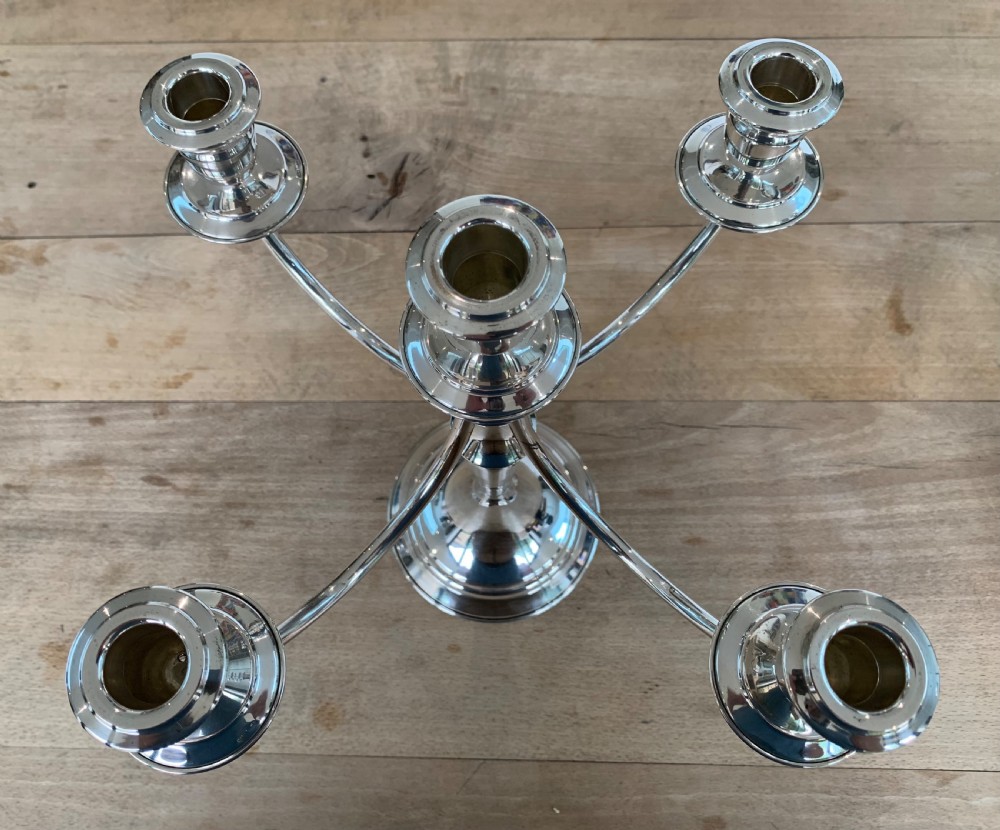 A polished silver candelabra featuring a central candle socket surrounded by four sweeping curved branches resting on a stepped round base. View VI