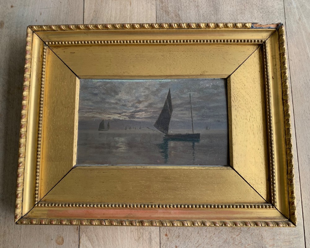 A 19th-century oil painting on board depicting sailing vessels on calm waters under an overcast sky, framed in a wide gilt frame.