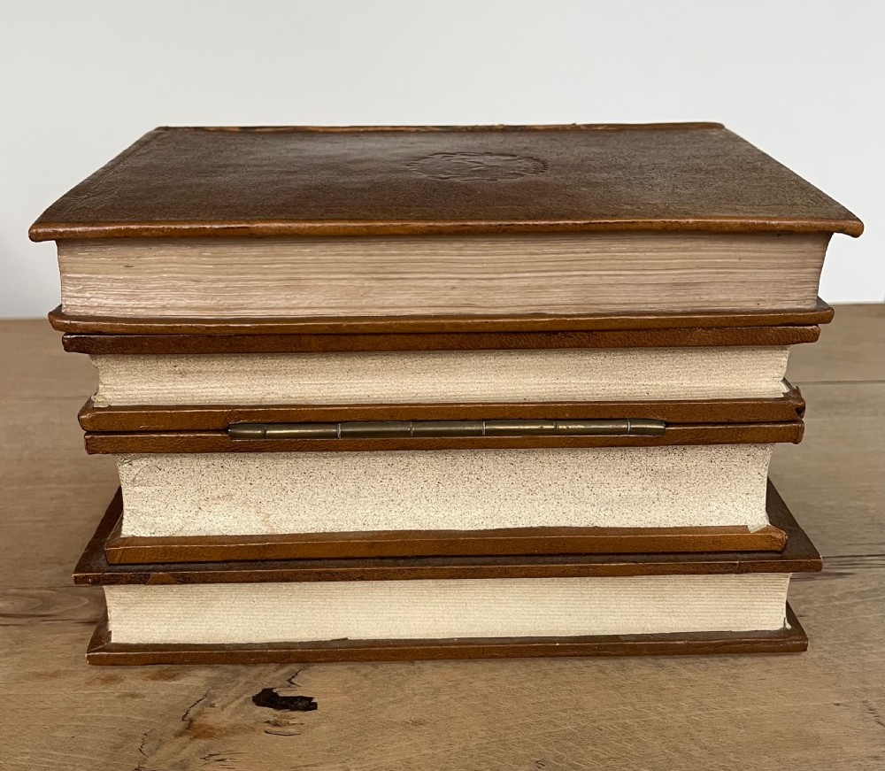 An open vintage warm brown leather box disguised as a stack of two gold-tooled books, featuring a fabric-lined interior with a brass support mechanism. View V