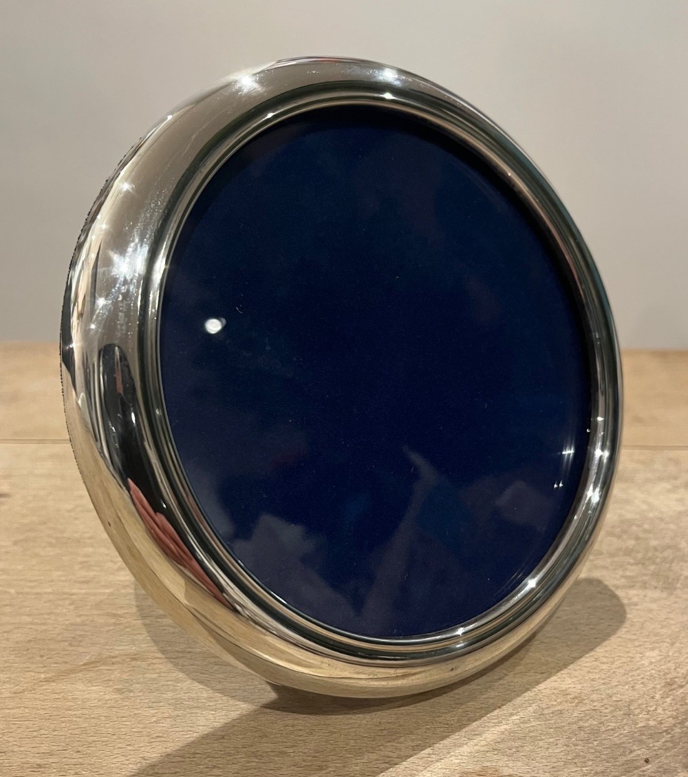 A circular vintage sterling silver photo frame featuring a convex polished bezel resting on a tabletop easel back.