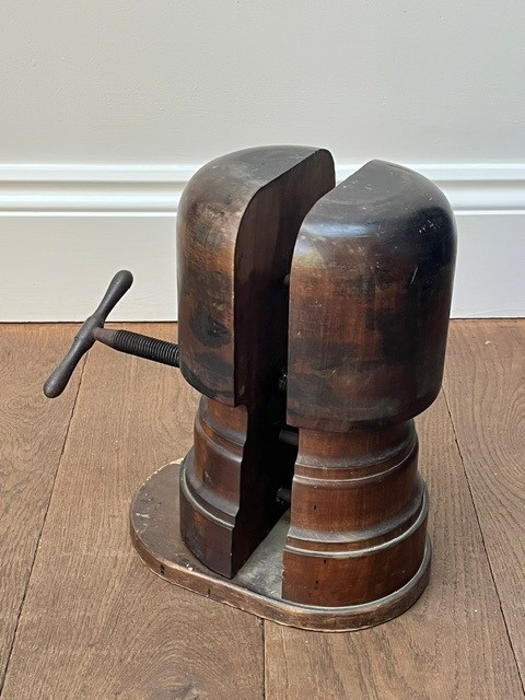 A nineteenth-century dark carved wooden hat stretcher featuring a split block mechanism operated by a threaded metal turn screw, set on an oval base.