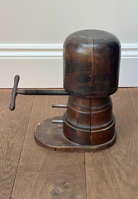 A nineteenth-century dark carved wooden hat stretcher featuring a split block mechanism operated by a threaded metal turn screw, set on an oval base. View II