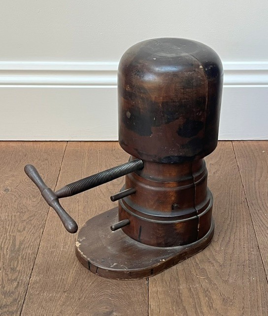 A nineteenth-century dark carved wooden hat stretcher featuring a split block mechanism operated by a threaded metal turn screw, set on an oval base. View III