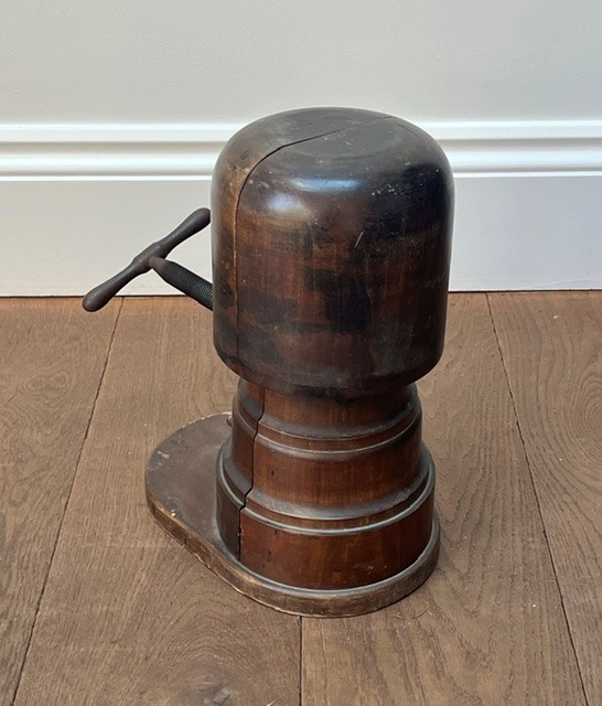 A nineteenth-century dark carved wooden hat stretcher featuring a split block mechanism operated by a threaded metal turn screw, set on an oval base. View IV