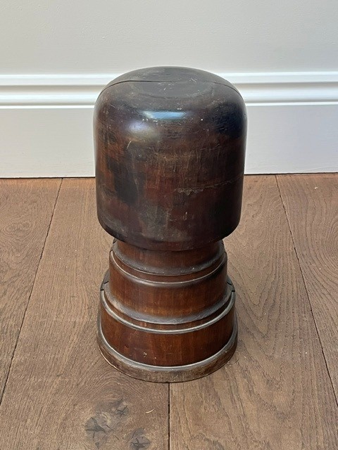 A nineteenth-century dark carved wooden hat stretcher featuring a split block mechanism operated by a threaded metal turn screw, set on an oval base. View V