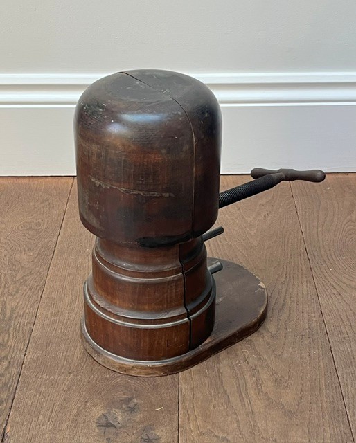 A nineteenth-century dark carved wooden hat stretcher featuring a split block mechanism operated by a threaded metal turn screw, set on an oval base. View VI