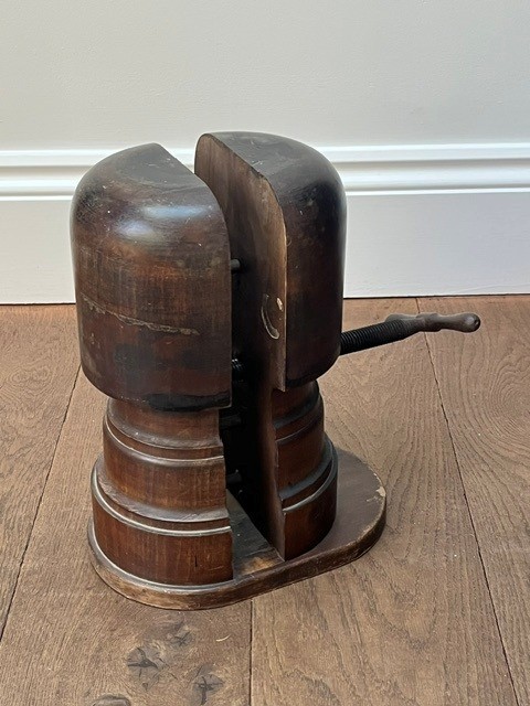 A nineteenth-century dark carved wooden hat stretcher featuring a split block mechanism operated by a threaded metal turn screw, set on an oval base. View VII
