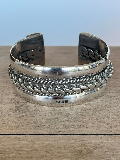 A wide, open-cuff solid silver bracelet featuring a central braided rope design flanked by smooth outer edges and stamped hallmarks. View II