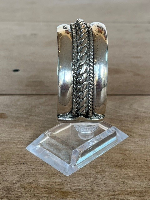 A wide, open-cuff solid silver bracelet featuring a central braided rope design flanked by smooth outer edges and stamped hallmarks. View V