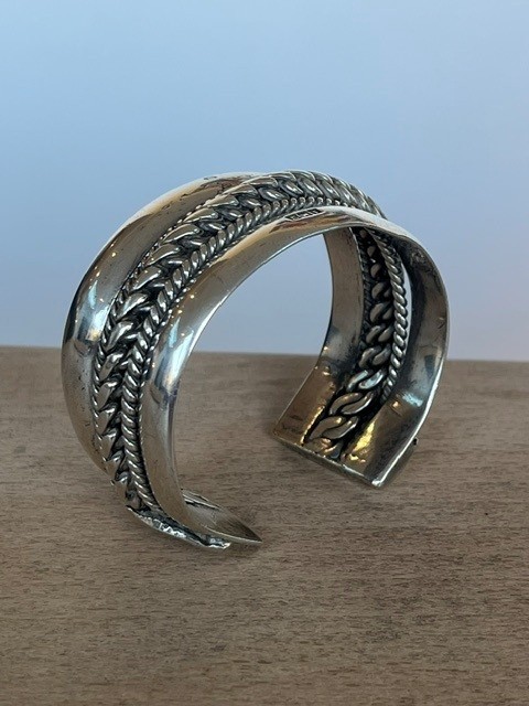 A wide, open-cuff solid silver bracelet featuring a central braided rope design flanked by smooth outer edges and stamped hallmarks. View VIII