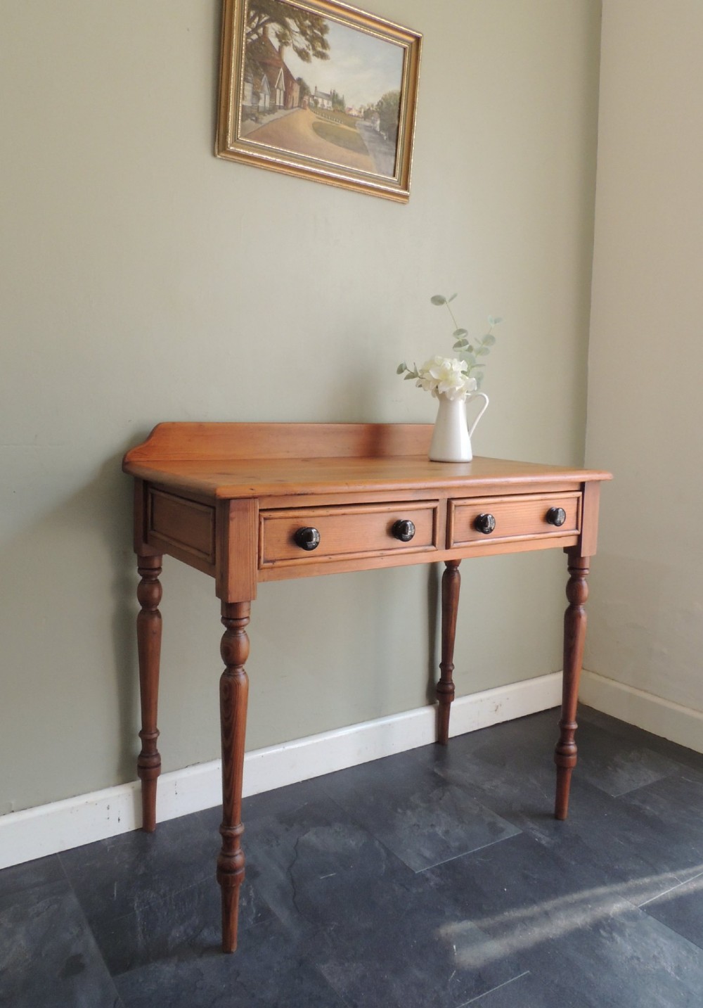 A Victorian solid pine hall table featuring a low gallery backboard, two drawers with dark round knobs, and four turned legs.