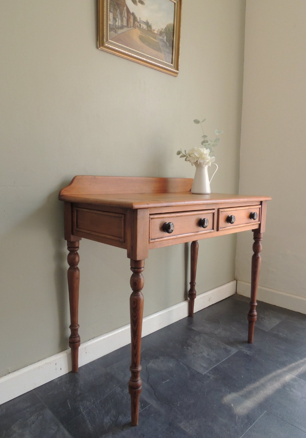 A Victorian solid pine hall table featuring a low gallery backboard, two drawers with dark round knobs, and four turned legs. View II