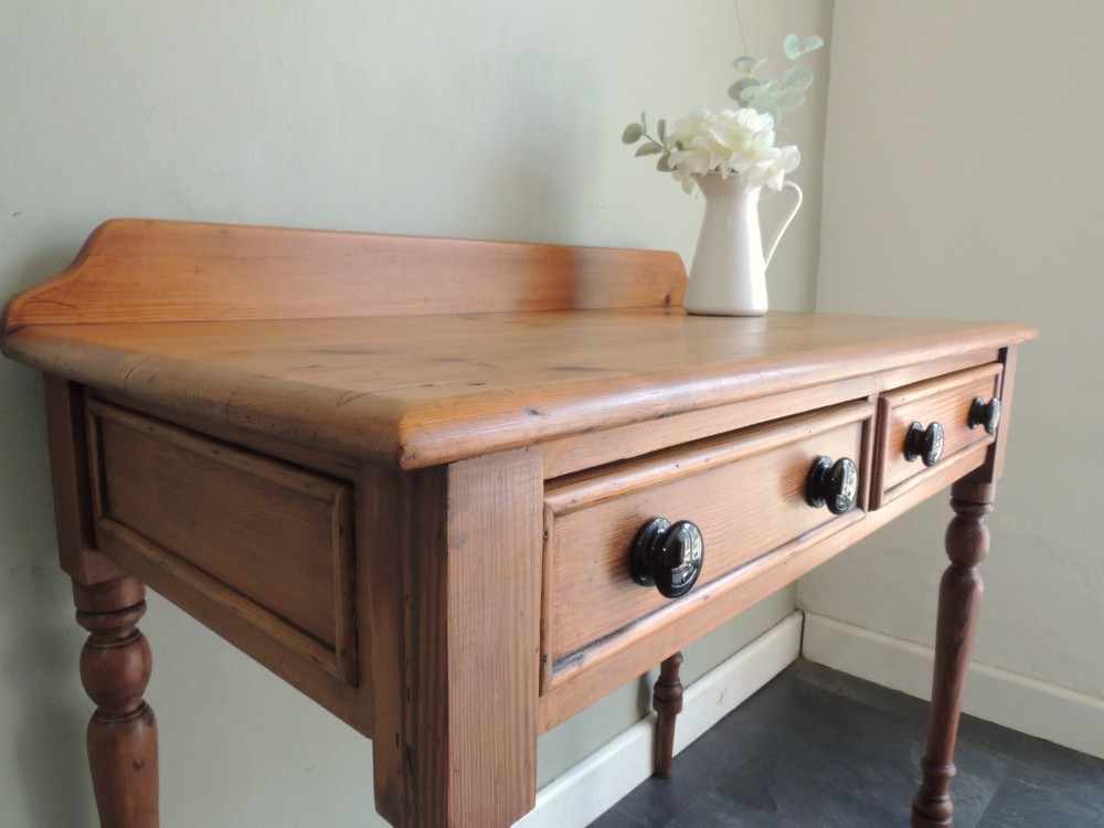 A Victorian solid pine hall table featuring a low gallery backboard, two drawers with dark round knobs, and four turned legs. View IV