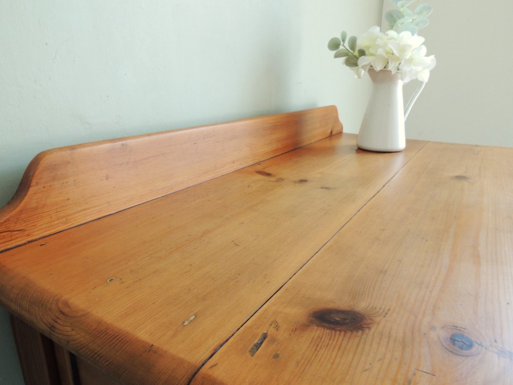 A Victorian solid pine hall table featuring a low gallery backboard, two drawers with dark round knobs, and four turned legs. View VII