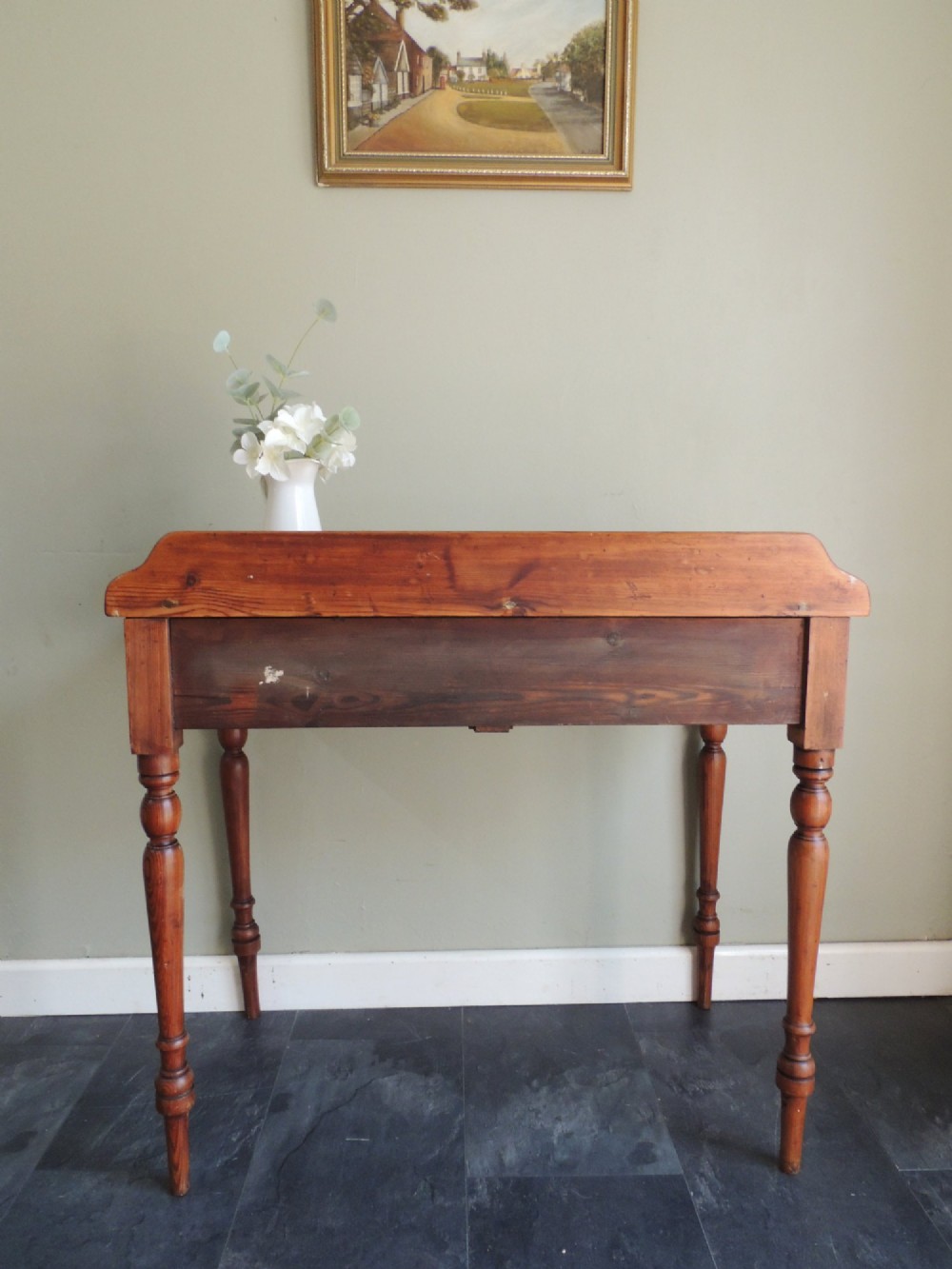 A Victorian solid pine hall table featuring a low gallery backboard, two drawers with dark round knobs, and four turned legs. View X