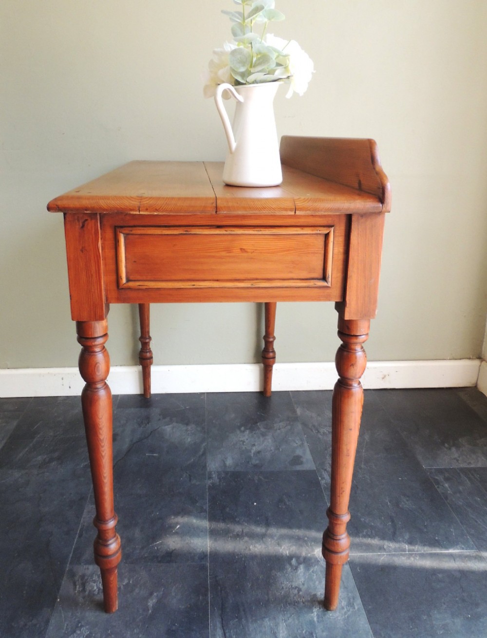 A Victorian solid pine hall table featuring a low gallery backboard, two drawers with dark round knobs, and four turned legs. View XI