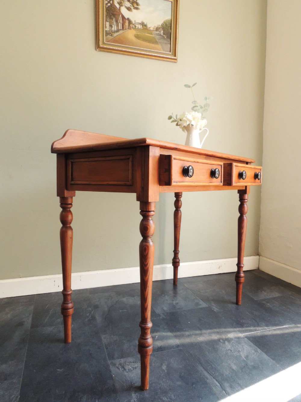 A Victorian solid pine hall table featuring a low gallery backboard, two drawers with dark round knobs, and four turned legs. View XIII