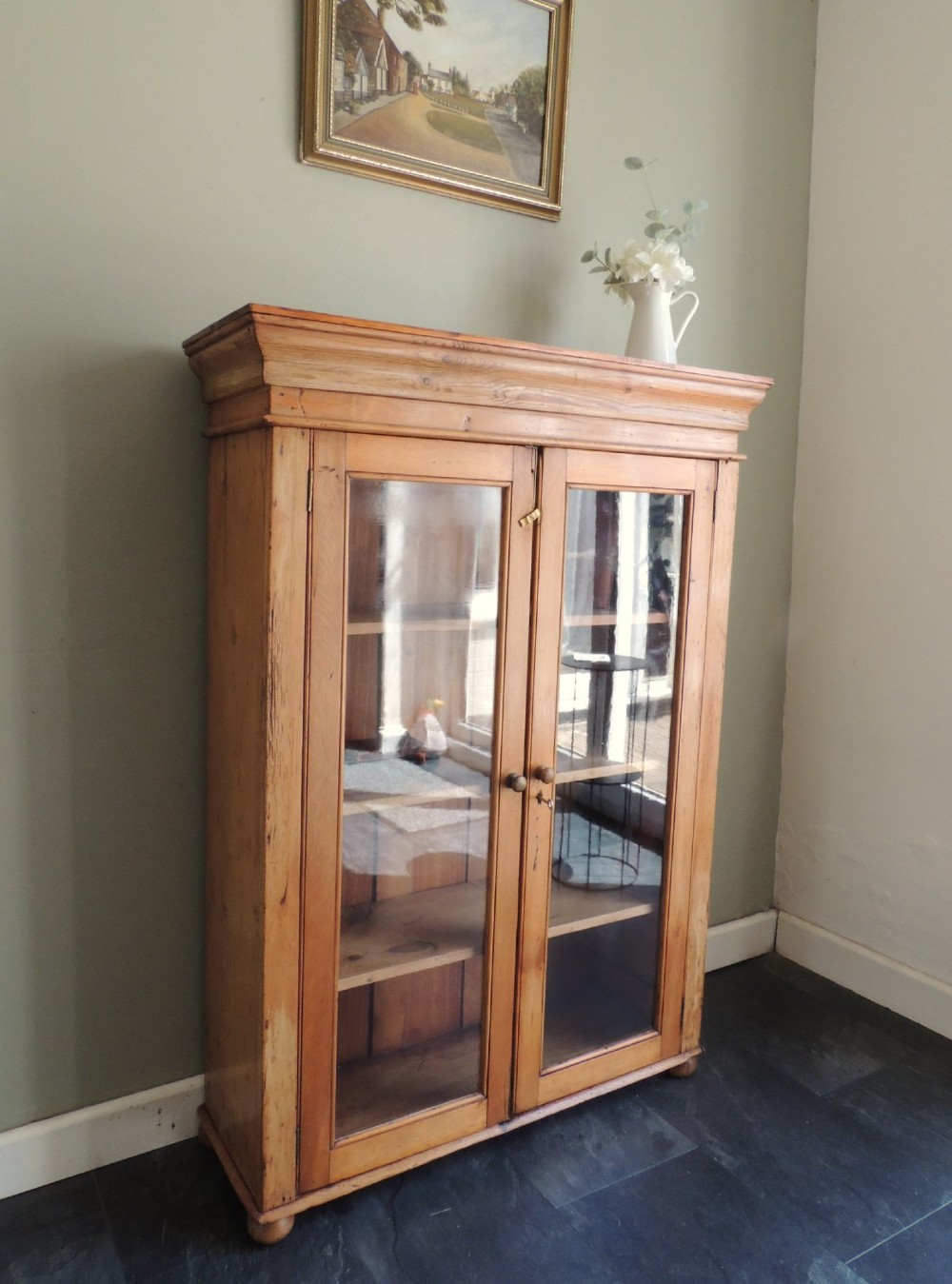 A Victorian solid pine glazed display cabinet featuring two full-length glass doors, wooden turned knobs, interior shelves, and a moulded top cornice.