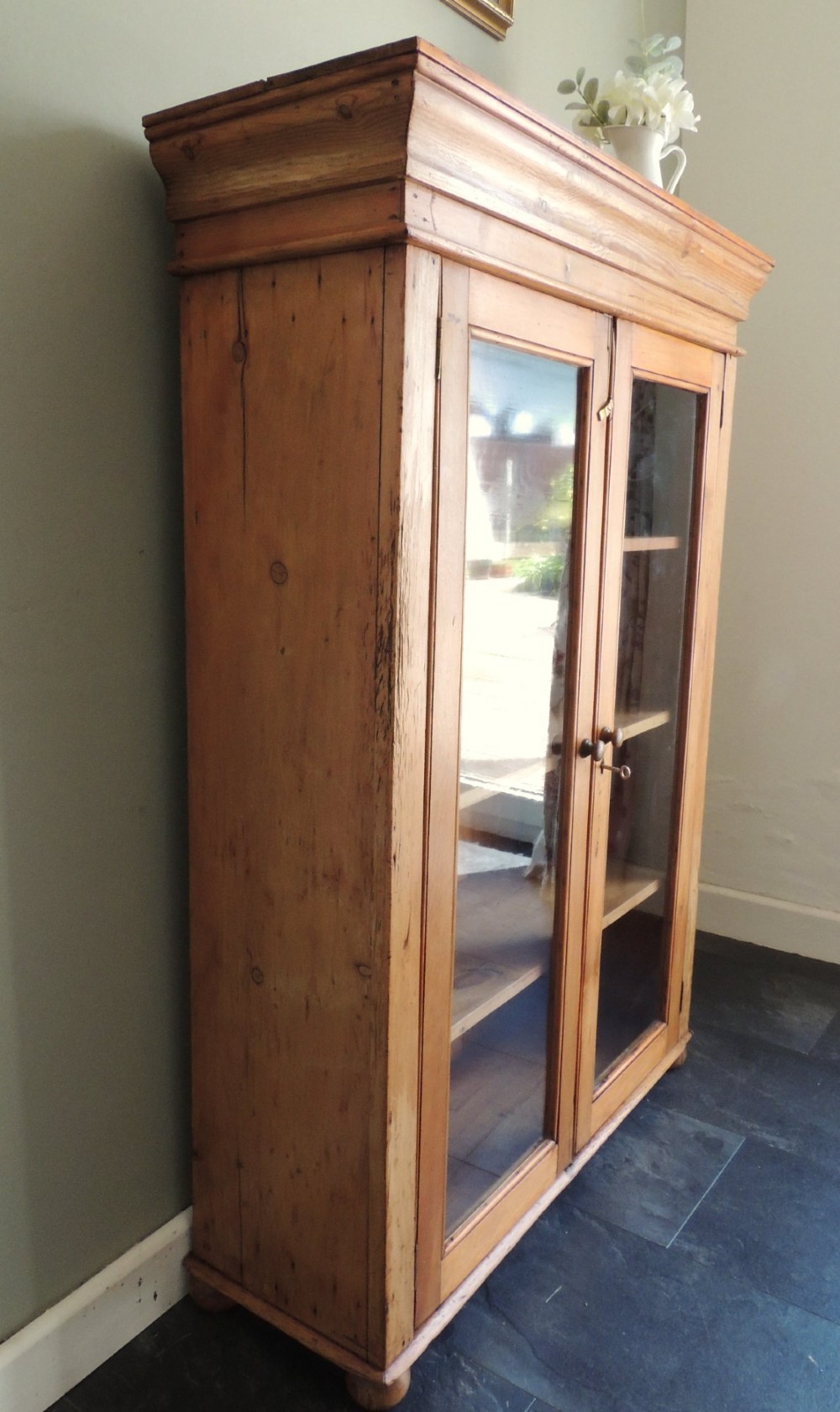 A Victorian solid pine glazed display cabinet featuring two full-length glass doors, wooden turned knobs, interior shelves, and a moulded top cornice. View II