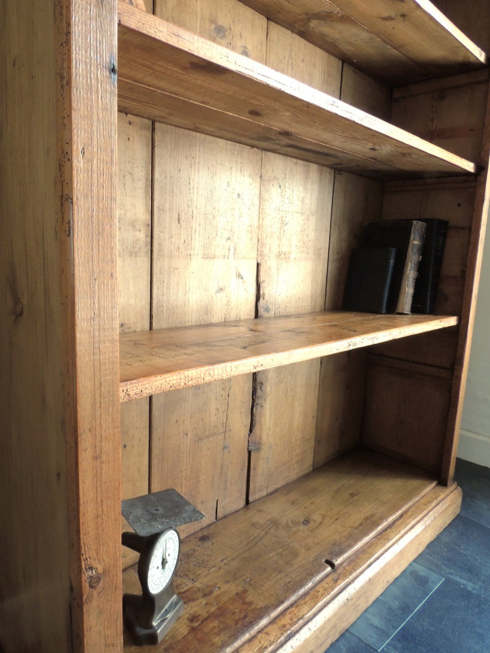 A tall Victorian open-front pine bookcase featuring four spacious shelves and a planked backboard resting on a solid plinth base. View VII