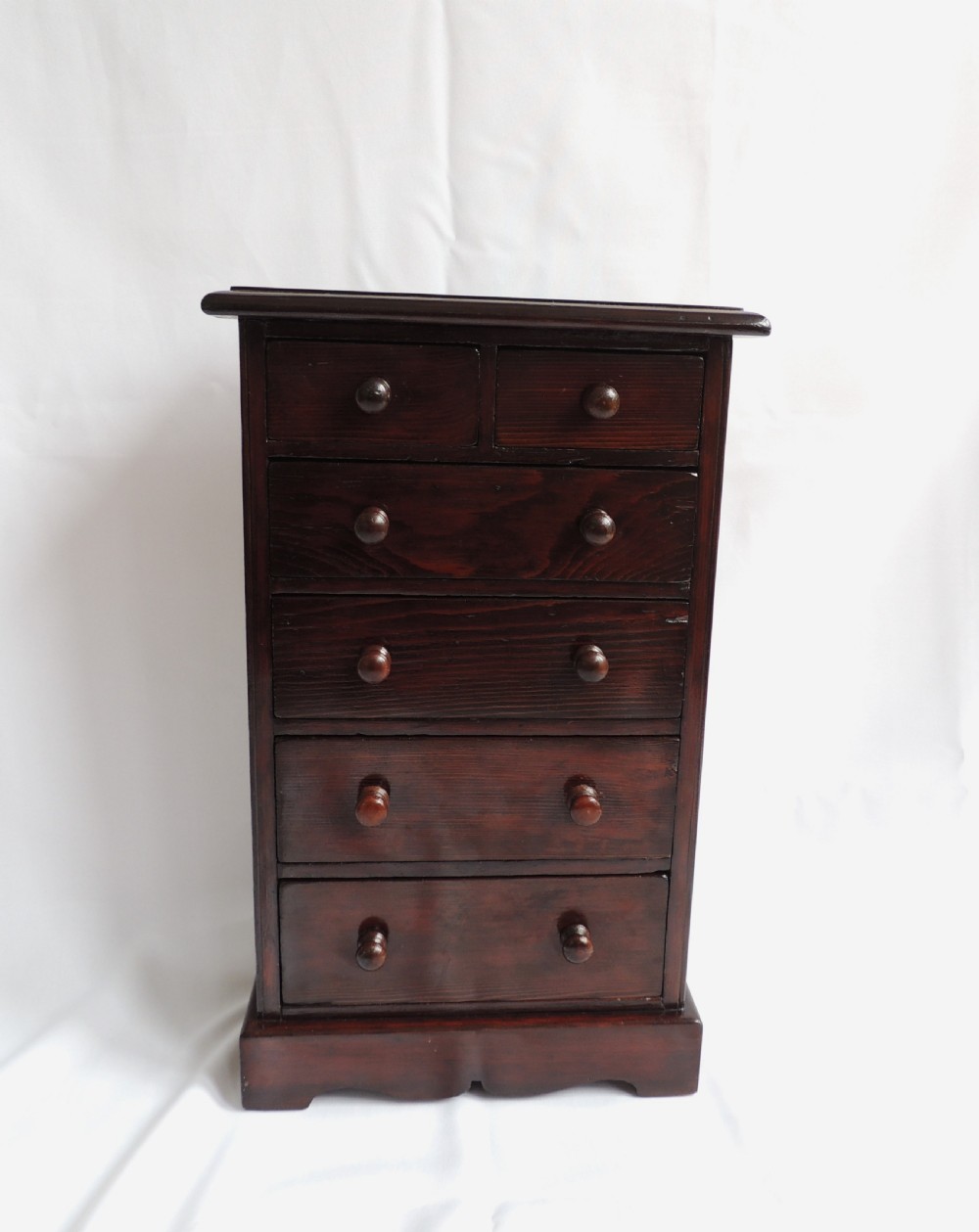 A dark stained pine Victorian miniature chest of drawers featuring six drawers with turned wooden knobs and a shaped plinth base. View III