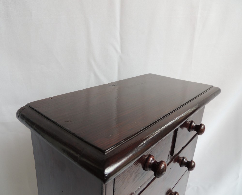 A dark stained pine Victorian miniature chest of drawers featuring six drawers with turned wooden knobs and a shaped plinth base. View VII
