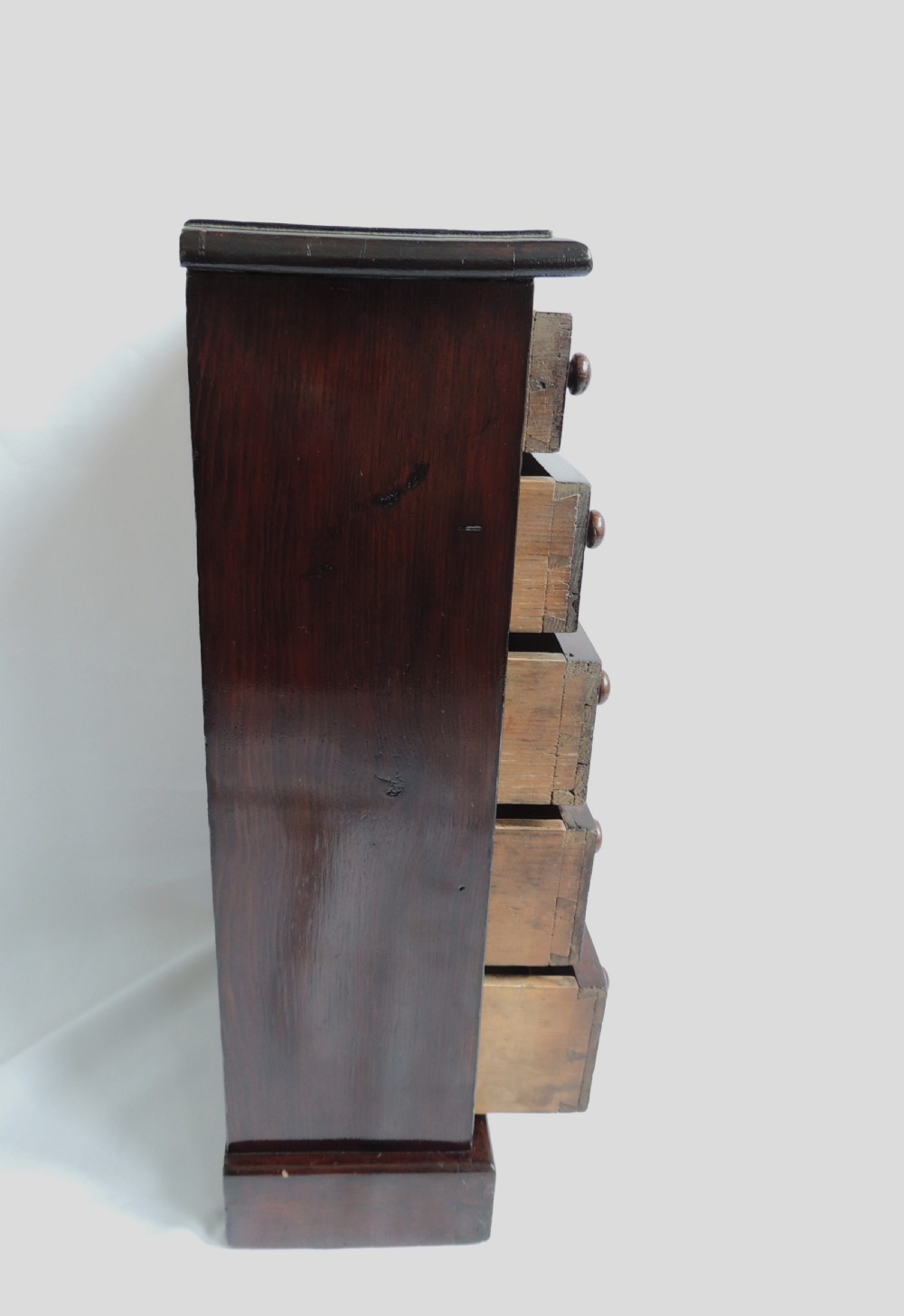 A dark stained pine Victorian miniature chest of drawers featuring six drawers with turned wooden knobs and a shaped plinth base. View VIII