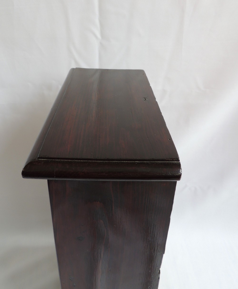 A dark stained pine Victorian miniature chest of drawers featuring six drawers with turned wooden knobs and a shaped plinth base. View XI