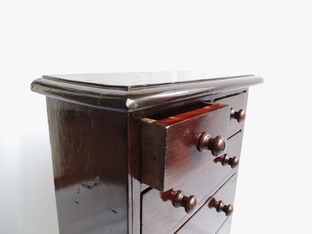 A dark stained pine Victorian miniature chest of drawers featuring six drawers with turned wooden knobs and a shaped plinth base. View XII