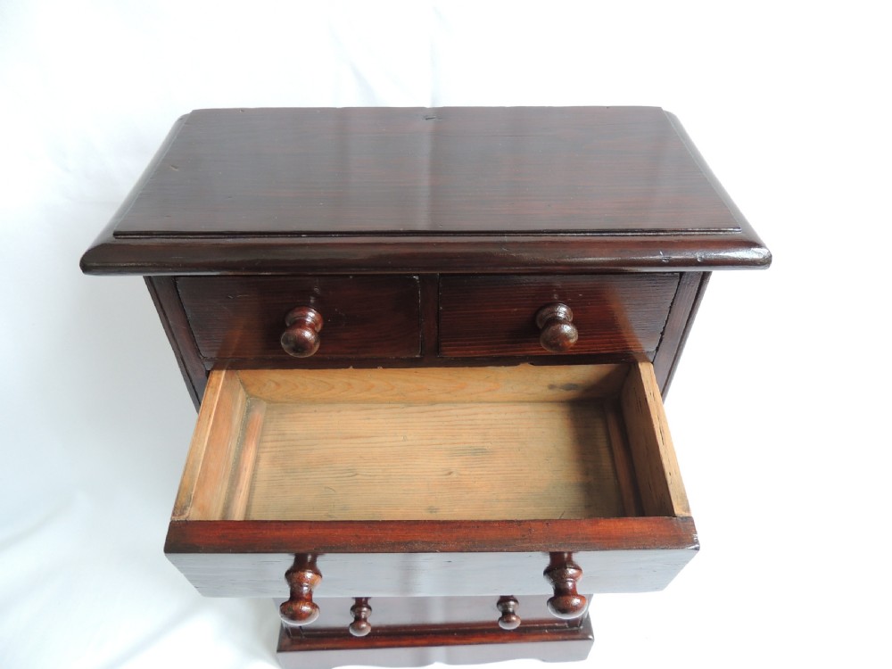 A dark stained pine Victorian miniature chest of drawers featuring six drawers with turned wooden knobs and a shaped plinth base. View XIII