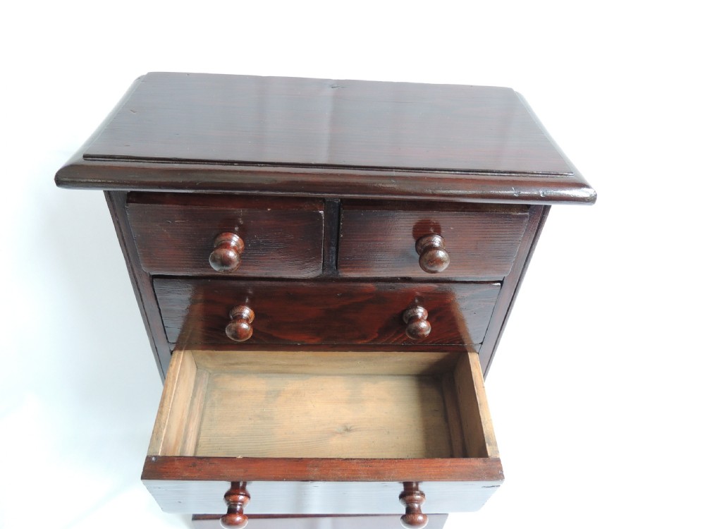 A dark stained pine Victorian miniature chest of drawers featuring six drawers with turned wooden knobs and a shaped plinth base. View XIV
