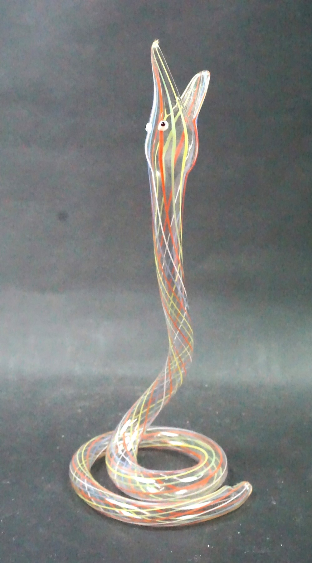 A clear glass lampwork sculpture of a snake coiled at the base with an upright open head, featuring internal red, yellow, and white cane striping.