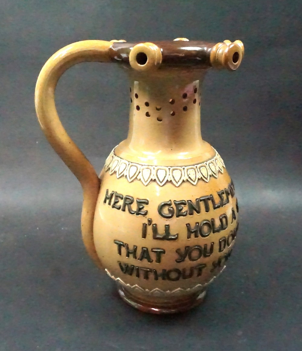 An antique Doulton Lambeth salt glazed stoneware puzzle jug featuring pierced neck detailing, an incised drinking verse on the body, and a dark brown handle. View II
