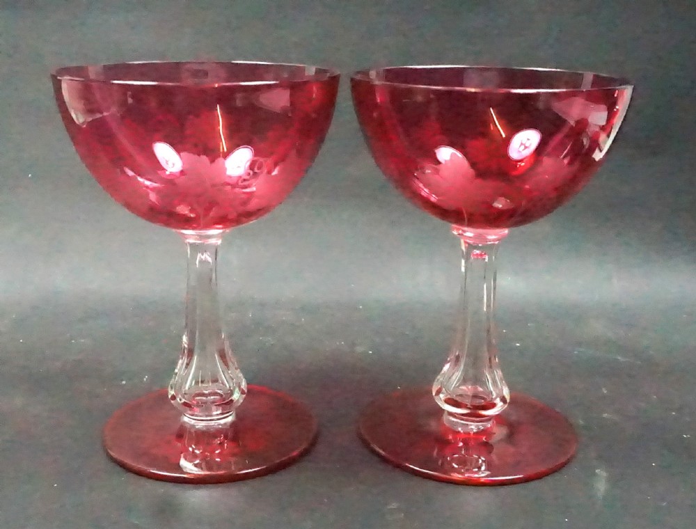 A pair of Victorian ruby red overlay crystal champagne coupes featuring etched fruiting vine motifs on clear knopped stems and circular red bases.