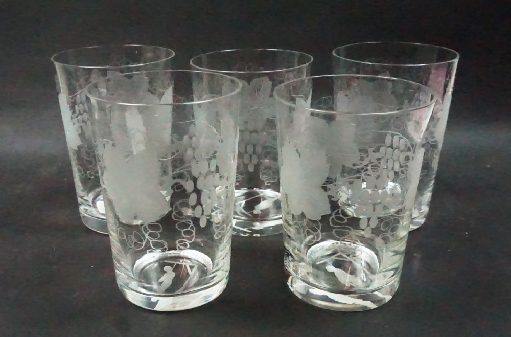 Set of clear glass tumblers engraved with fruiting vine patterns and a miniature novelty figure at the interior base.